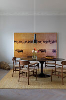 Round dining table in dark wood with chairs, in front of large art print on the wall