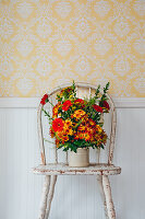 Herbstlicher Blumenstrauß mit Gerbera, Chrysanthemen (Chrysanthemum) und Dahlien (Dahlia) auf einem abgenutzten Stuhl