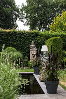 Ruhiger Gartenbereich mit kleinem Teich, Buddha-Statue und Pflanzen in Töpfen