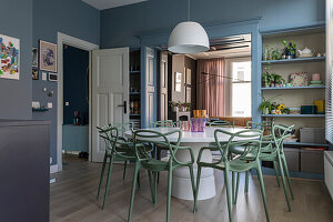 Dining room with green designer chairs and round white table against blue walls