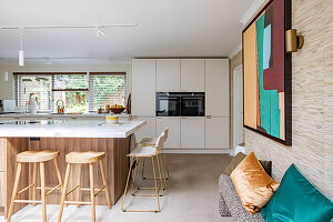 Modern open-plan kitchen with wooden island, bar stools and abstract art