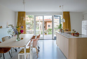 Open-plan kitchen with large dining table, yellow curtains and view of the garden