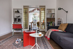Wohnzimmer mit rotem Beistelltisch, grauem Sofa und orientalischem Teppich
