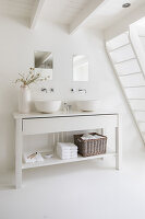 White bathroom with double sinks and storage basket under staircase