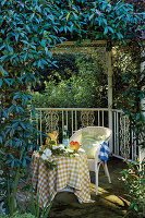 White rattan chair and laid table in a pergola overgrown with plants in the garden