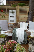 Sitzecke mit Kissen, Tierfell und Textilien auf der Terrasse, im Hintergrund Sichtschutz aus Holzlatten
