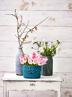 Tulpen, weiße Ranunkeln und Zweig in Vasen mit gehäkeltem Bezug