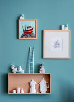 Wall shelf with miniatures and illustrations on a turquoise-coloured wall