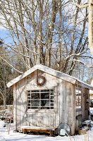 Wooden hut in snowy garden in front of bare trees in winter