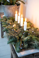 Adventsgesteck aus Tannenzweigen mit weißen Kerzen auf Holzbank