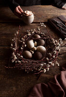Weidenkranz als Osternest geformt mit Hühner- und Wachteleiern auf rustikalem Holztisch