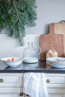 Kitchen worktop with plates, fir branches, wooden chopping boards and glass jug with milk