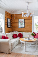 White corner sofa with red cushions in living room with wooden walls and candlestick