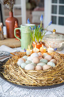 Osterdeko: Nest aus Stroh mit gefärbten Ostereiern und Kerzen auf Tisch