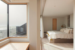 Schlafzimmer mit Meerblick und großem Eckfenster, Holzboden und Textilien in hellen Tönen