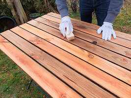 Man spreads oil on wooden table with brush