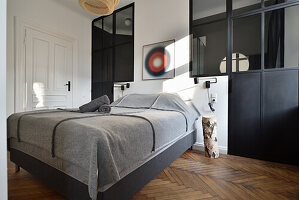 Schlafzimmer mit grauer Tagesdecke, schwarzem Raumteiler und Fischgrätparkett