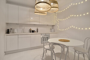 Küchenzeile und Essbereich in Weiß mit Pendelleuchten und Lichterketten