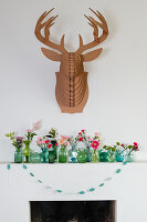 Flower arrangements in green glass vases on mantelpiece with deer head decoration