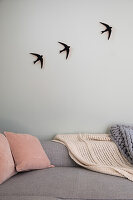 Light grey sofa with pink cushions, knitted blankets and three swallows as wall decoration