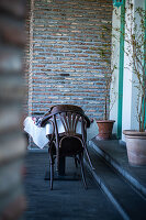 Holzstühle und Tisch auf rustikaler Terrasse mit Ziegelwand und Topfpflanzen
