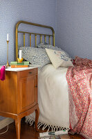 Messingbett und Vintage-Nachttisch in Schlafzimmer mit blauer Tapete mit Streublumen