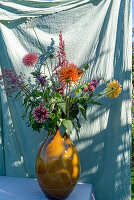 Bunter Blumenstrauß in bernsteinfarbener Vase vor grünem Hintergrund