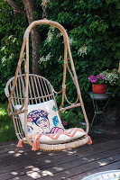 Rattan hanging chair with cushions on wooden terrace in the garden