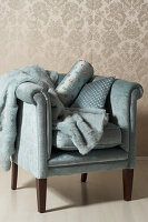 Blue armchair with fur blanket and patterned cushions in front of baroque wallpaper