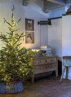 Illuminated Christmas tree next to rustic chest of drawers and wall pictures