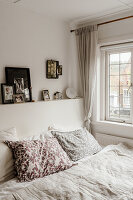 Bedroom with white bed linen and patterned pillows, with family photos on headboard