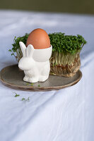 Bunny-shaped egg cup with egg next to cress on plate