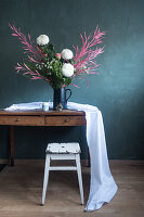 Rustic wooden table with flower arrangement in front of green wall