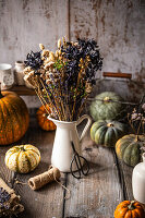 Dried flowers in a white vase on a wooden table with pumpkins and craft materials, autumn decoration