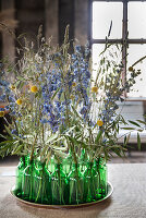 Dried meadow flowers in green glass bottles on a round tray