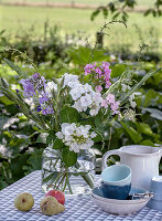 Summer bouquet of flowers in glass vase on garden table with ceramic crockery