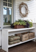 White sideboard with planter box, cushions and wooden boxes on veranda