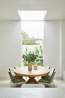 Round wooden table with light green velvet chairs under large skylight