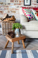 Kleiner Holzschemel mit Kiefernzapfen und Hortensienvase neben Sofa