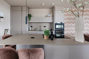 Modern kitchen with island, pink velvet chairs and patterned wallpaper