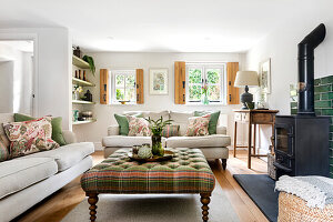 Bright living room with fireplace, cream-coloured sofas and chequered ottoman