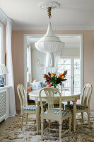 Round, antique dining table with chequered chairs under a white chandelier