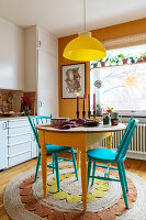 Buntes Esszimmer mit gelber Lampe, gelbem Esstisch und türkisfarbenen Stühlen