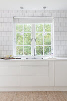 Bright kitchen with white tiles and pendant lights by the window