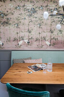 Essbereich mit Kranich-Tapete, Holztisch, grüner Bank mit Lehne und grünen Samtstühlen