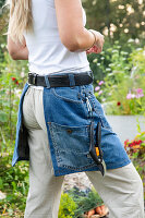 Gärtnerin mit Jeans-Schürze und Gartenschere im Blumenbeet