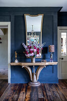 Wooden console with lavish bouquet of flowers and mirror in front of blue wall