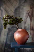 Bronze vase with olive branches in front of antique wallpaper