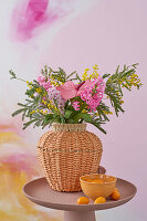 Spring bouquet with flamingo flower (anthurium), hyacinth and mimosa in a woven vase on a round table