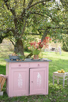 Pink chest of drawers with fern print in the garden under an apple tree